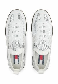 Zapatillas blancas transpirables con parte superior de malla, superficie texturizada, suela gris en contraste y diseño sin cordones. Presenta una etiqueta con el logo en el talón.