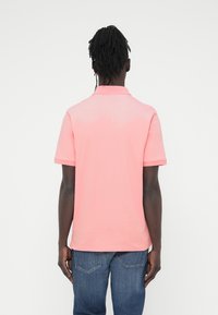 Πόλο πουκάμισο σε ανοιχτό ροζ βαμβάκι, με κοντά μανίκια, ριμπ γιακά και πλευρικές σχισμές, συνδυασμένο με μπλε τζιν παντελόνι, από πίσω όψη.