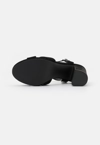 Sandal con tacco alto nero con tomaia in suede, cinturino alla caviglia regolabile, suola testurizzata e design del tacco cilindrico.