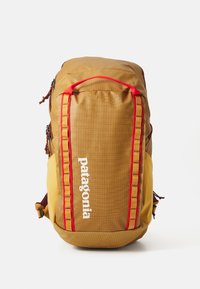 Bruine en gele rugzak met een gestructureerd oppervlak, rode accenten en een voorkantlogo. Heeft ritsen en verstelbare schouderbanden.