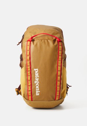 Bruine en gele rugzak met een gestructureerd oppervlak, rode accenten en een voorkantlogo. Heeft ritsen en verstelbare schouderbanden.