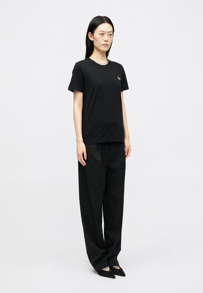 Μαύρο βαμβακερό μπλουζάκι με κοντά μανίκια και στρογγυλή λαιμόκοψη, συνδυασμένο με μαύρες φαρδιές παντελόνες και μυτερές μπαλαρίνες. Μινιμαλιστικός σχεδιασμός.