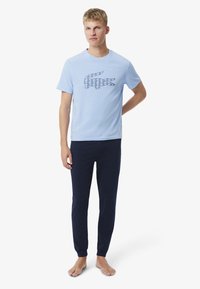T-shirt bleu clair avec un logo crocodile géométrique bleu foncé, associé à un pantalon jogger bleu marine. Mélange de coton, coupe décontractée.
