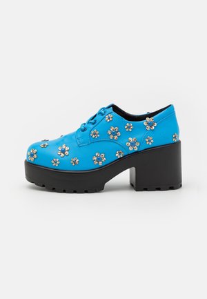 Chaussures compensées en cuir bleu avec semelle épaisse noire, ornées de strass floraux sur la partie supérieure et avec un design à lacets.