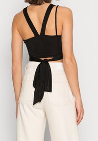 Svart cropped top med knytning bak, med breda justerbara remmar och en jämn yta. Kombineras med ljusa högmidjade byxor.