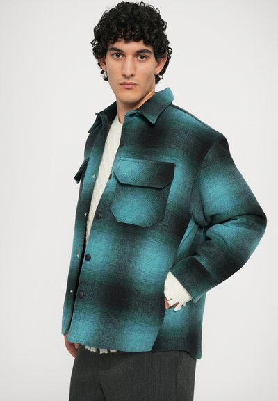 Camicia in flanella a scacchi teal e nera, con chiusura a bottoni, due tasche sul petto e colletto. Tessuto testurizzato.