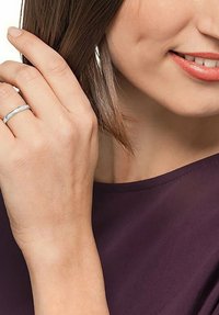 Silberner Ring mit geradem Design, verziert mit kleinen klaren Steinen, getragen an der linken Hand. Hand und Ring vor einem sanften lila Hintergrund.