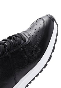 Sneaker in pelle nera con punta perforata, lacci neri e suola in gomma bianca. Presenta una finitura testurizzata e una silhouette elegante.