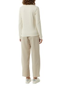 Helles cremefarbenes Langarmoberteil mit dünnen beigen Streifen, kombiniert mit lockeren, hellbeigen Hosen und weißen Sneakers, von hinten betrachtet.
