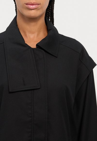 Black coat with a structured collar, made of a smooth fabric. Features include a hidden closure and shoulder accents for a tailored look.