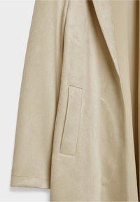Manteau beige à manches longues avec une poche verticale fendue et une texture douce ressemblant à du daim, présenté sur un fond clair.