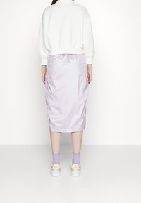 Sudadera blanca con mangas abullonadas combinada con una falda midi lila. La falda tiene una textura ligeramente arrugada y una cintura fruncida.