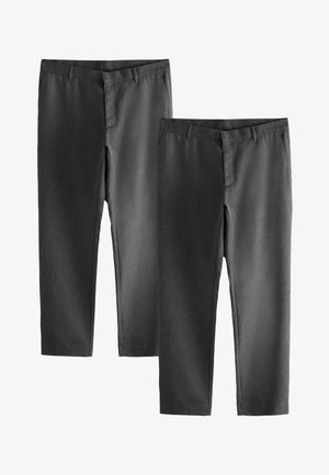 Mann trägt hellblaues Langarmhemd, dunkelgraue Hose und schwarze Schuhe, steht vor einem schlichten beigen Hintergrund.