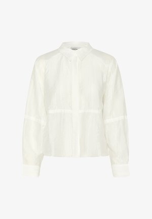 Blouse blanche à manches longues avec un col à boutons, présentant un tissu texturé et un design cropped, complétée par des manches à poignets.
