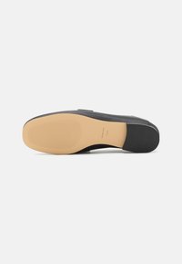 Zwarte leren schoen met een gladde bovenkant, rubberen zool en een gestructureerde beige buitenzool. Voorzien van minimale stiksels en een instapontwerp.