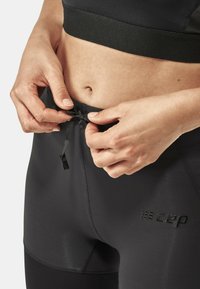 Black athletic leggings with a drawstring waist, featuring a textured logo accent and smooth material, highlighting a fitted design.