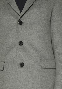Blazer grigio in lana con revers a punta, quattro bottoni neri e due tasche frontali con finitura in tessuto testurizzato.