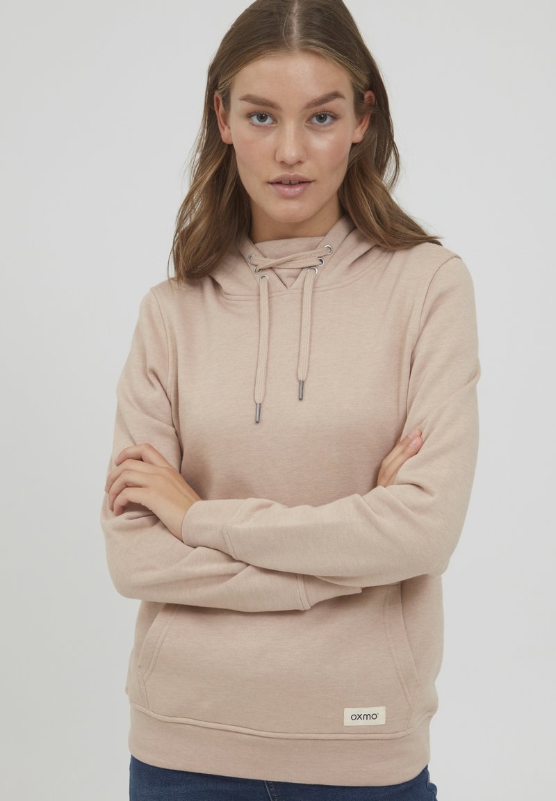 Beige hoodie med dragsko i huvan, känguruficka och ribbade manschetter. Har en liten logotagg vid nederkanten. Mjuk material och avslappnad passform.