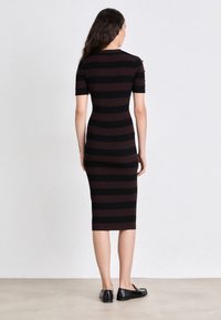 Vestito aderente, lungo fino al ginocchio, con righe orizzontali nere e borgogna scuro. Realizzato in materiale a coste, con maniche corte, abbinato a scarpe nere flat.