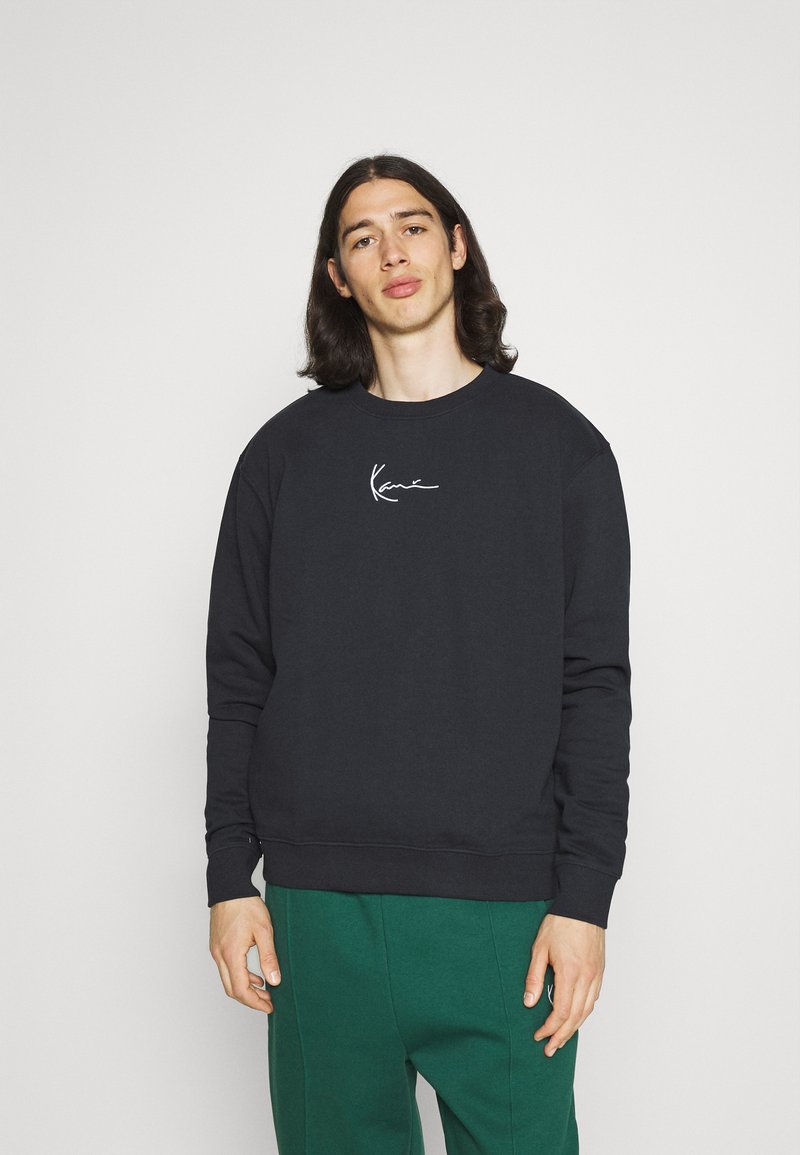 Sweatshirt negru cu guler rotund, având un logo alb semnătură pe piept, fabricat dintr-un material moale, cu mansete și tiv cu nervuri.