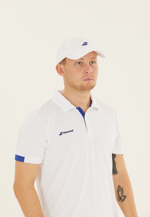 Hvid polo shirt med blå detaljer, der har en to-knap placket og Babolat-logoet på venstre bryst. Hvid kasket fuldender looket.