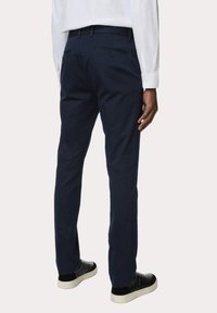Pantalones chinos azul marino con un corte recto, que cuentan con dos bolsillos traseros y una textura suave. Combinados con zapatillas negras y una camisa blanca de manga larga.