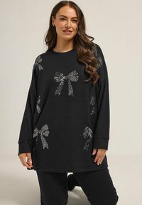 Schwarzer Pullover mit langen Ärmeln, der mit silbernen Pailletten-Schleifen-Designs verziert ist. Weicher Stoff mit einer lockeren Passform und rundem Ausschnitt. Maschinenwaschbar.