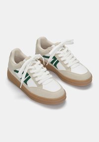 Sneakers z beżowym zamszem i białą skórzaną cholewką, zielonymi akcentami, białymi sznurówkami i brązową gumową podeszwą. Okrągły design noska.