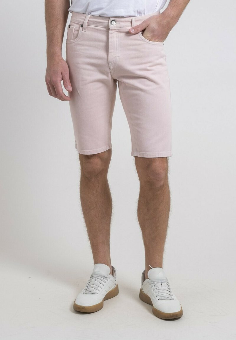Shorts en denim rose clair avec une coupe droite, cinq poches et une fermeture à bouton métallique, associés à des baskets blanches et une chemise unie.