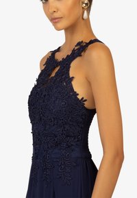 Navy blue dress with floral lace detailing on the bodice, featuring a keyhole neckline and textured fabric, complements a sleek silhouette.