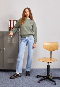 Grey oversized sweatshirt, light blue straight-leg jeans, black shoes with a thick sole. Wooden chair beside a metal filing cabinet.