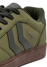 Olive green sneaker with synthetic upper, gray accents, perforated detailing, and brown rubber sole. Features logo and contrasting stitching.