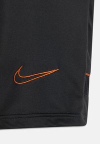 Pantalones cortos deportivos negros con un logo de Nike bordado en naranja. El material es liso, con un panel de malla para mayor transpirabilidad.