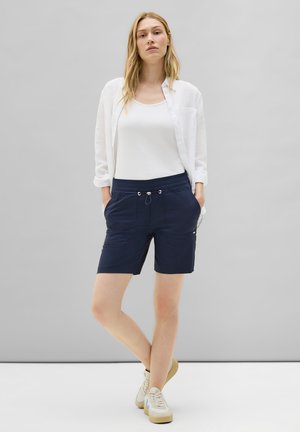 Shorts bleu marine en tissu léger avec une taille élastique, un cordon de serrage et des poches latérales. Associés à un débardeur blanc et à une chemise.