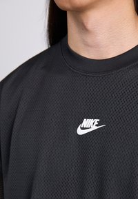 Persona vistiendo una camiseta deportiva de malla negra de Nike, mostrando el área del pecho superior y la parte inferior de la cara.
