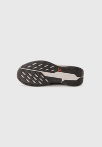 Semelle de chaussure de course noire avec un motif texturé, présentant des accents gris et un logo proéminent en orange. Caoutchouc durable avec un design antidérapant.