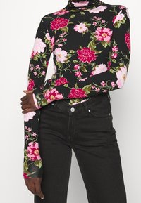 Långärmad polotröja i svart med ett blommönster i rosa och grönt. Mjuk tyg med tajt passform och förlängda ärmslut.