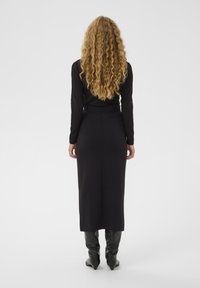 Garš melns kleita ar piegrieztu krūšu daļu, garām piedurknēm un taisnu, līdz potītēm garu svārku. Modelis valkā gludas melnas zeķubikses līdz ceļiem.