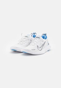Biele športové topánky s textúrovaným pleteným zvrškom, svetlo modrými akcentmi a šedým logom Swoosh. Sú vybavené polstrovanou podrážkou a dizajnom na šnurovanie.