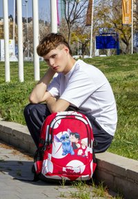 Mochila roja con un diseño de dibujos animados que presenta personajes. Hecha de tela, tiene un compartimento principal, bolsillos laterales de malla y un logo.