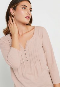Haut à manches longues rose clair avec un col en V et cinq boutons, présentant des plis verticaux et une texture douce.