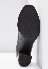 Bottine en cuir noir avec une finition lisse, un bout rond, un talon bas et une semelle en caoutchouc à motifs. Présente des accents de couture sur les côtés.