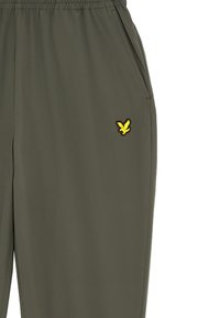 Olijfgroene broek met een elastische tailleband, zijzakken en een gele adelaar logo aan de linkerkant. Glad materiaal met een losse pasvorm.