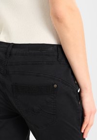 Svarta jeans med texturerade bakfickor, med dekorativ sömnad och metallaccenter. Slätt tyg med en åtsittande design.