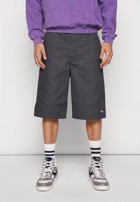 Pantaloni corti grigi con vestibilità rilassata, in cotone, con un logo discreto sulla parte bassa. Indossati con calze bianche e nere a righe e sneakers alte.