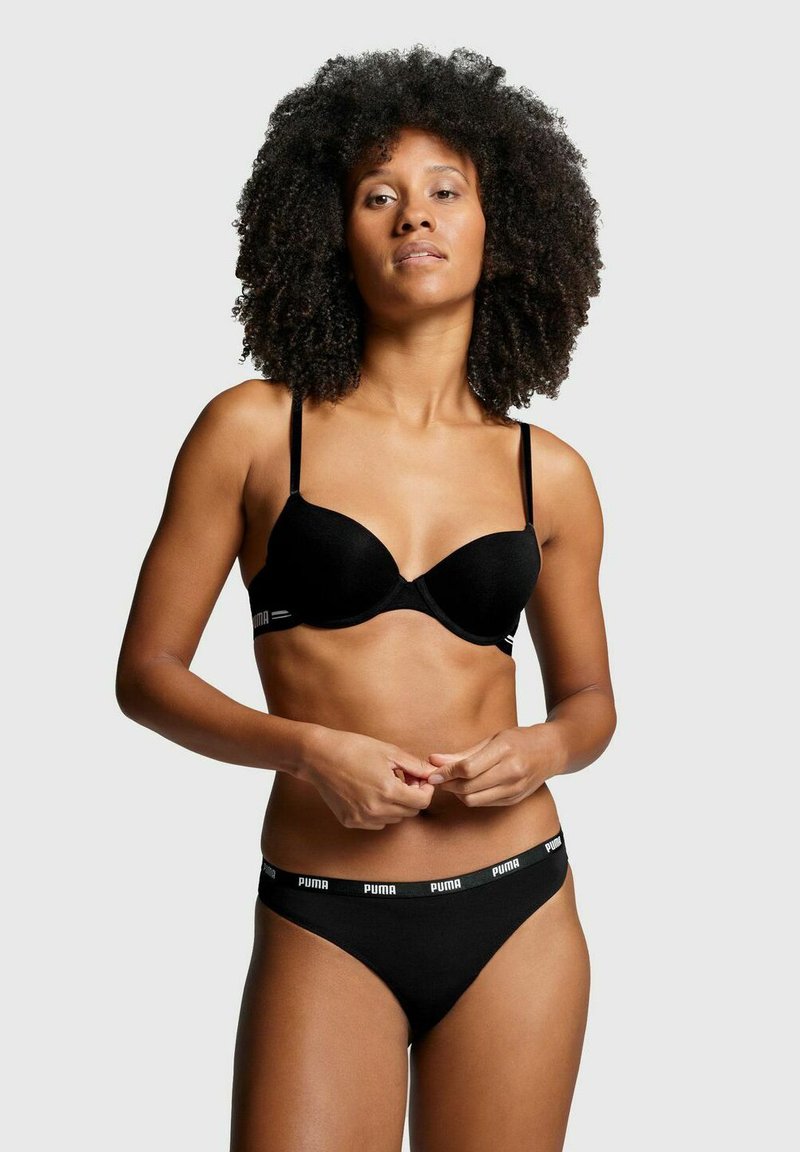 Schwarzer Bh und passender Tanga mit verstellbaren Trägern und elastischem Bund, der das Puma-Logo trägt. Glatte Textur, minimalistisches Design.