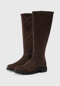 Bottes en suède marron foncé jusqu'au genou avec des semelles en caoutchouc noir à crampons, bouts ronds et zips sur les côtés, présentées sur un fond uni.