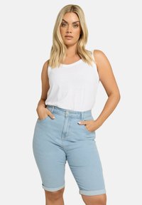 Ljusblå denimshorts med uppvikt fåll, hög midja och knappstängning. Bärs med en enkel vit ärmlös topp.
