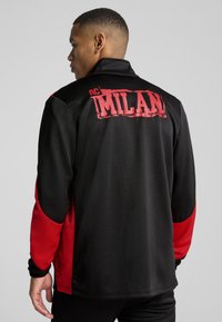 Mustmust ja punane AC Milan jope pikkade varrukatega, kõrge kaelusega ja seljaosas on suured logo trükitud julgete punaste tähtedega.