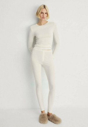White long-sleeve top and fitted leggings made from a soft, lightweight material; includes a button detail at the waist. Fuzzy slippers.